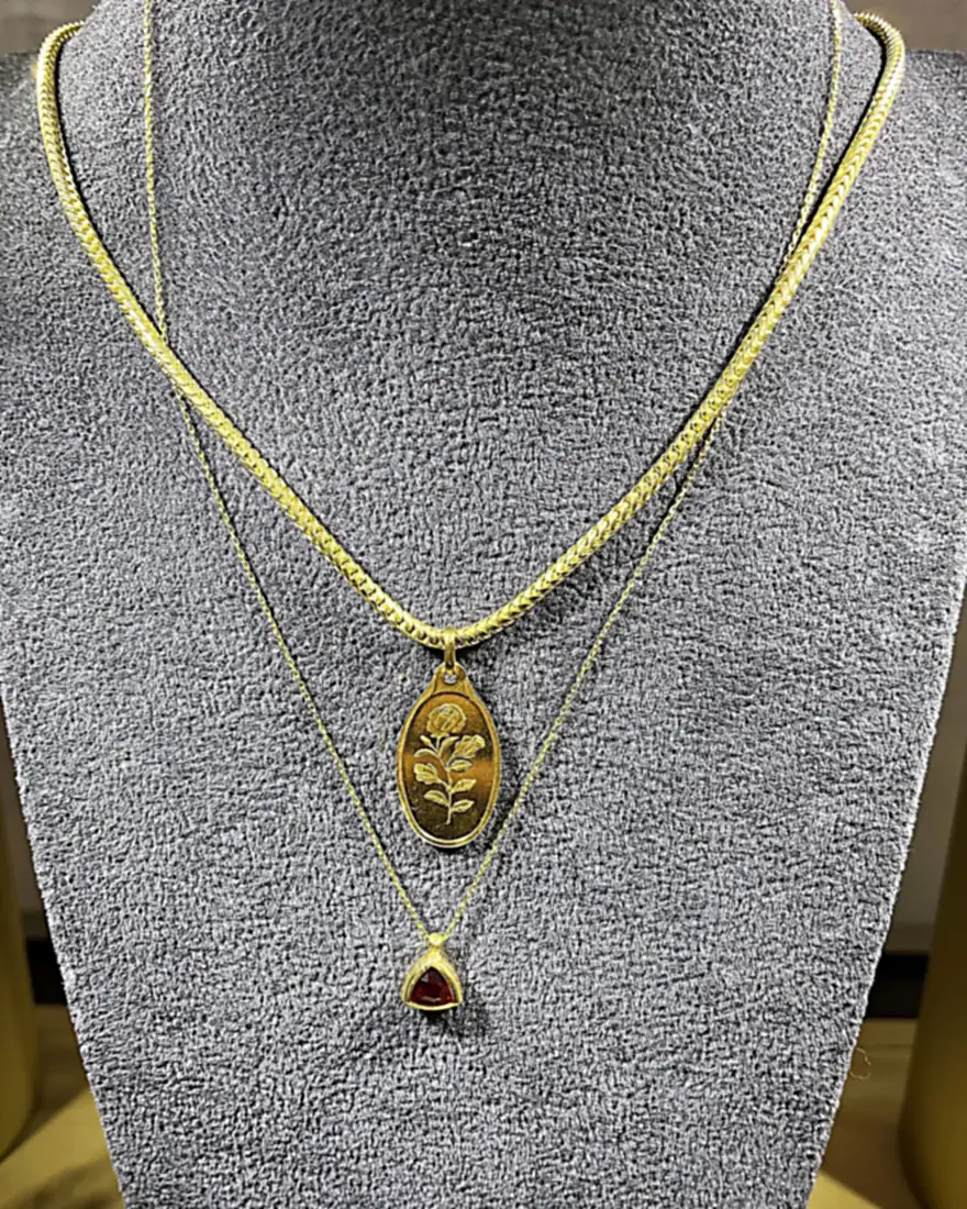 Layered gold necklaces — an engraved rose medallion and a garnet drop on a velvet bust