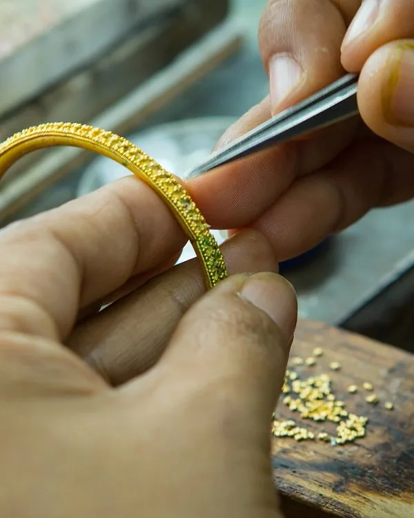 Hands finishing a hand-textured gold bangle with tweezers at the workbench