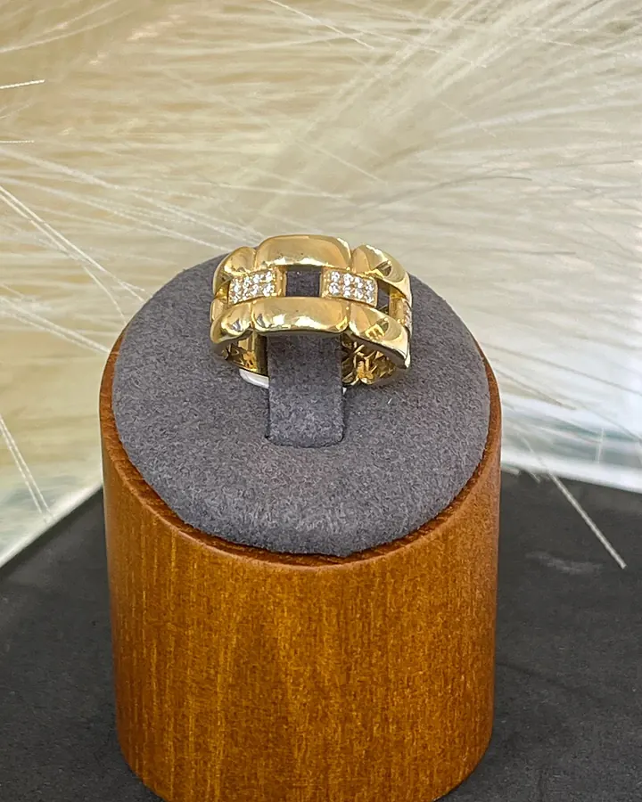 Gold link ring set with pavé diamond bars, on a wooden pedestal